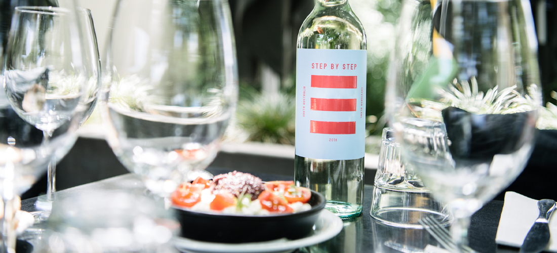 Step by Step wine bottle surrounded by wine glasses and plate of food 